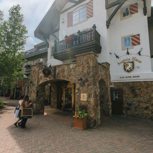 A quaint building with a stone entrance, white walls, turquoise trim, and potted plants; sunny day and clear skies.