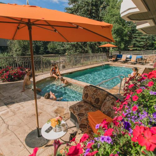 A sunny poolside scene with orange umbrellas, colorful flowers, and a swimming pool sparkling by a patio area.