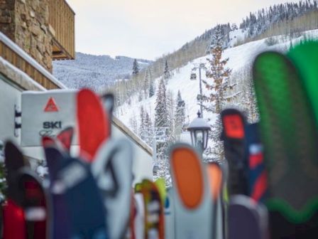 A row of colorful snowboards planted upright outside a ski lodge, with snowy mountains in the background and a crisp winter scene.