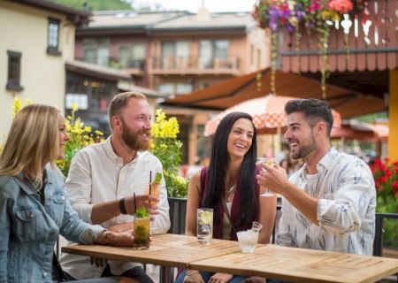 Four friends sit at a picnic table outside, chatting and smiling as they share a meal.