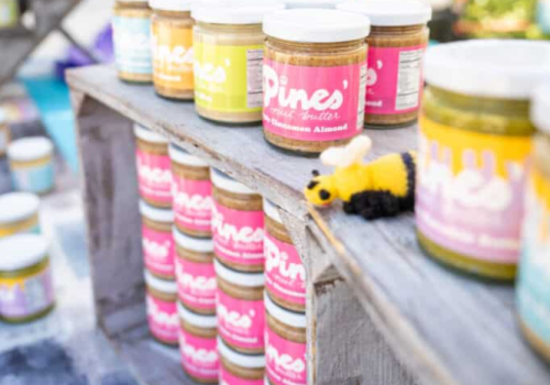 Assorted pint-sized paint jars with colorful labels arranged on a weathered wooden railing, bright hues ready for art projects.