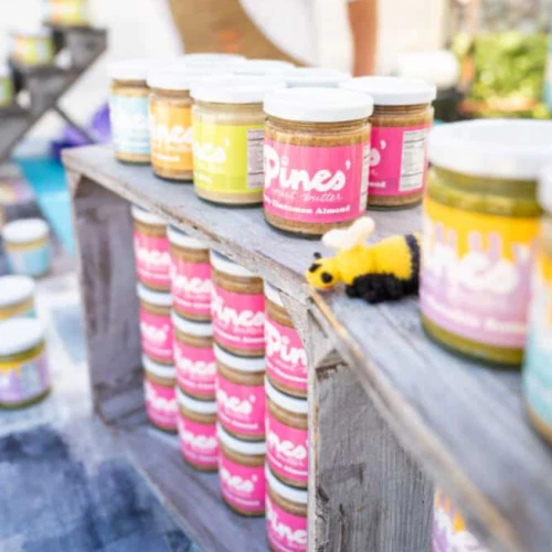 Assorted pint-sized paint jars with colorful labels arranged on a weathered wooden railing, bright hues ready for art projects.
