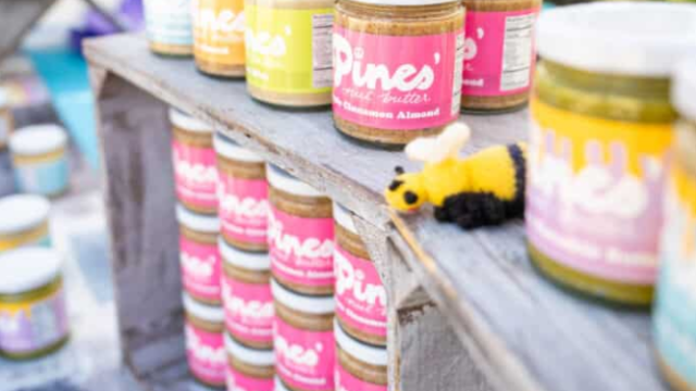 Assorted pint-sized paint jars with colorful labels arranged on a weathered wooden railing, bright hues ready for art projects.