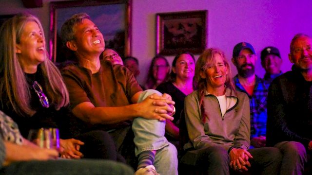 A group of people watching a show or performance in a cozy, dimly lit room, smiling and laughing together.