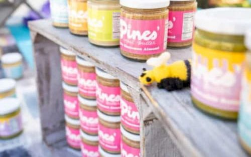 A row of pastel-colored jars on a wooden railing, bright labels, a small bee/bumble toy, outdoor market vibe.