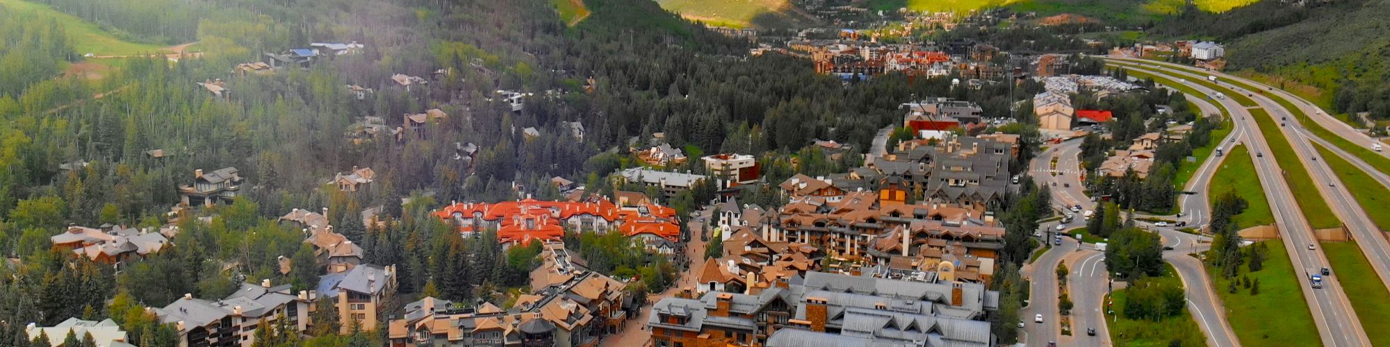 A scenic mountain town with colorful houses, winding streets, and a highway cutting through, nestled among green hills under a bright sky.
