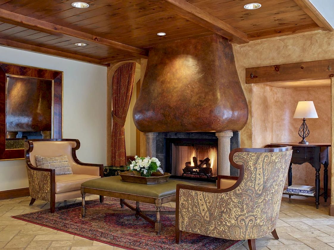 A cozy living room with a modern fireplace, rustic wood ceiling, and cushioned seating around a coffee table, warm lighting, and a rug.