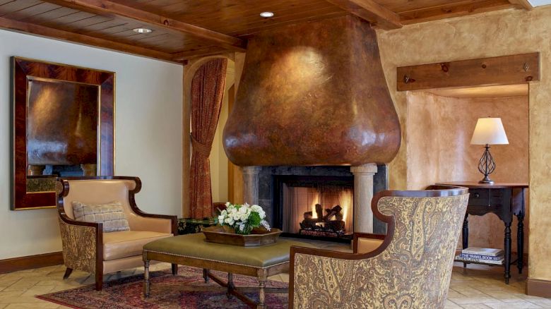 A cozy living room with a modern fireplace, rustic wood ceiling, and cushioned seating around a coffee table, warm lighting, and a rug.